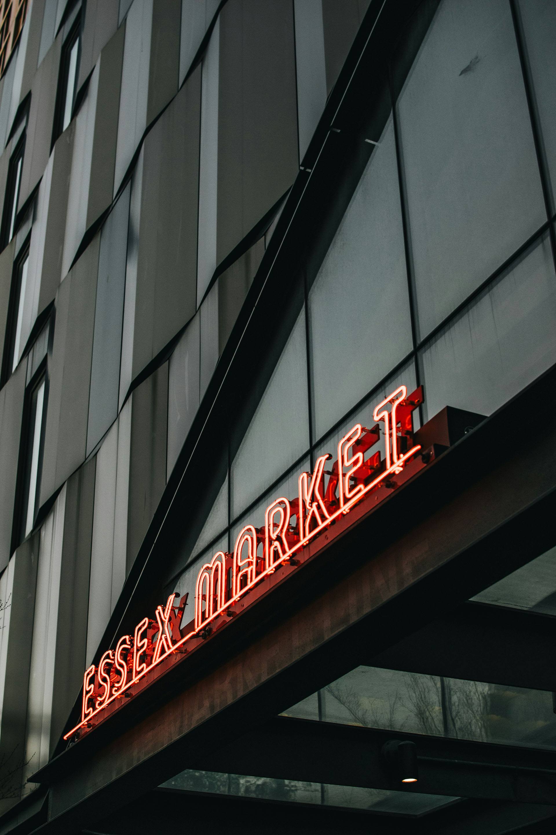 A neon sign that says "lessex market" hangs on a building.